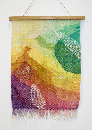 A tapestry in a rainbow of colors hangs on a white wall. 